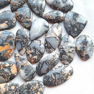 May include: A collection of 15 black, white, and gold gemstone cabochons. The cabochons are all teardrop shaped and have a speckled pattern.