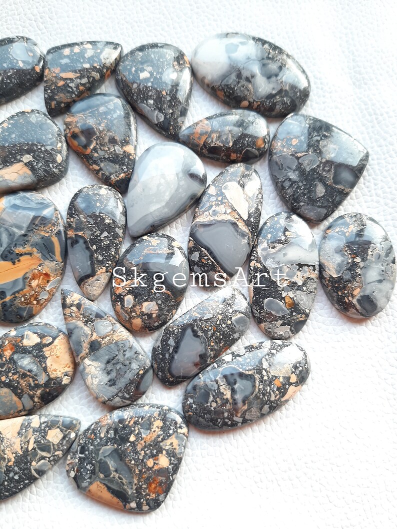 May include: A collection of 15 black, white, and gold gemstone cabochons. The cabochons are all teardrop shaped and have a speckled pattern.