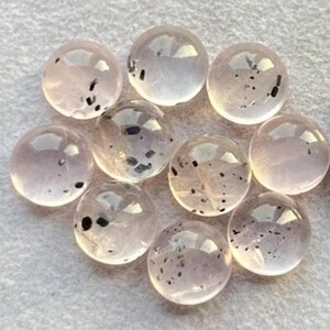 Könnte beinhalten: Zehn runde, durchscheinende rosa Cabochons mit schwarzen Einschlüssen. Die Cabochons sind glatt und poliert.