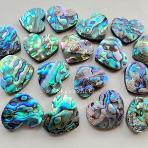 May include: A collection of 15 iridescent abalone shell heart-shaped cabochons. The cabochons are a mix of blue, green, and purple colors.