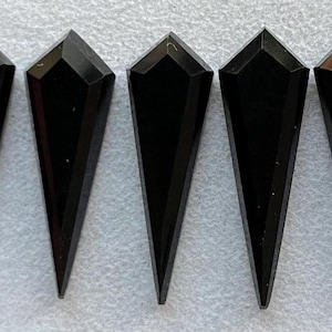 Puede incluir: Seis colgantes de cristal negro puntiagudos y facetados. Los colgantes son todos del mismo tamaño y forma, y están dispuestos en fila.