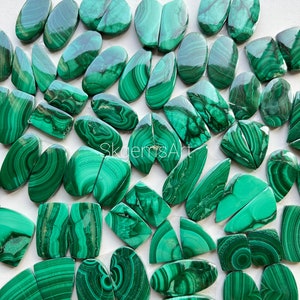 May include: A collection of green malachite cabochons, some are oval shaped, some are rectangular, and some are freeform. The stones have a variety of patterns and textures.