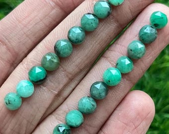 May include: A strand of faceted green gemstone beads with black inclusions. The beads are round and have a polished finish.