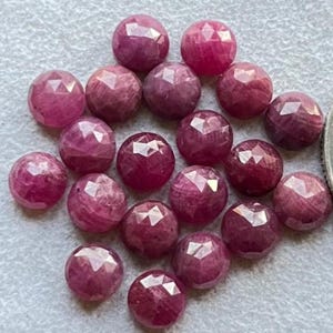 May include: A collection of faceted, round gemstones in varying shades of pink and red. The gemstones have a polished, reflective surface, and are arranged closely together. The overall effect is a display of vibrant, natural beauty.