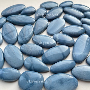 Puede incluir: Una colección de 20 cabujones de ópalo azul, de diferentes tamaños y formas. Las piedras tienen un acabado liso y pulido y muestran una variedad de tonos azules.