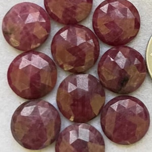 May include: Nine faceted, round gemstones in varying shades of red and pink are arranged closely together. The gemstones have a polished, reflective surface with multiple facets, creating a sparkling effect. The gemstones are likely for jewelry making.