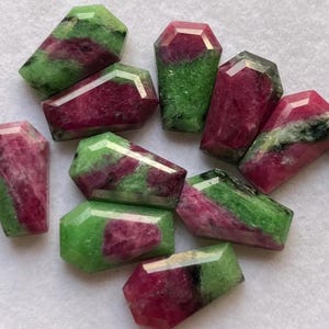 Peut inclure: Collection de perles en pierres précieuses facettées en forme de cercueil. Les perles présentent une combinaison de couleurs vertes et rouge foncé. Les pierres précieuses sont disposées en gros plan, mettant en valeur leurs formes et variations de couleurs uniques.