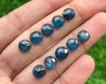 May include: Ten faceted blue gemstones, likely aquamarine, are arranged in a row on a hand. The gemstones are round and have a slightly irregular shape.