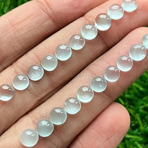 May include: A collection of round, translucent, light blue gemstones. The gemstones are arranged in two rows on a hand.