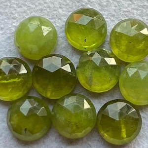 以下が含まれることがあります： 10個のファセットカットされた緑色の宝石。それぞれに独特のインクルージョンのパターンがあります。石は丸く、研磨されています。