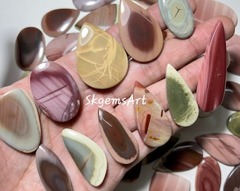 May include: A collection of 18 polished, teardrop-shaped, and rectangular natural stone cabochons in various shades of brown, pink, green, and white. The stones have a layered, striated pattern and are arranged on a hand.