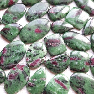 Op de afbeelding: Een verzameling van 17 groene, zwarte en roze edelsteen cabochons. De stenen zijn ovaal, peervormig en rechthoekig. De stenen zijn gepolijst en hebben een gladde, glanzende afwerking. SkgemsArt.
