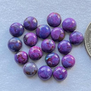 May include: A collection of 16 purple and blue cabochon stones, each with a unique pattern of swirls and veins. The stones are approximately 1/2 inch in diameter and are arranged in a random pattern on a white surface.
