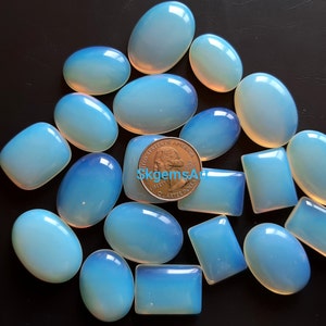 May include: A collection of 18 oval and rectangular cabochon opal gemstones in various sizes. The stones are a pale blue color with a slight iridescent sheen. A US quarter is included for scale.