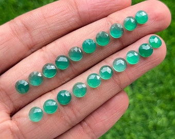May include: A collection of 18 round, faceted green gemstones. The stones are arranged in two rows on a hand.