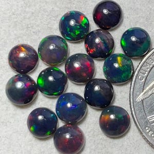 Könnte beinhalten: Eine Sammlung von 14 runden schwarzen Opal-Cabochons mit irisierenden grünen, roten und blauen Blitzen. Die Opale haben einen Durchmesser von etwa 6 mm.