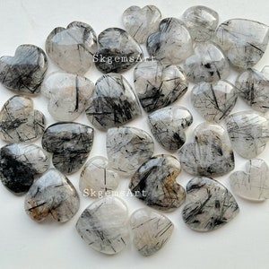Könnte beinhalten: Eine Sammlung von 20 herzförmigen schwarzen Turmalin-Kristall-Cabochons. Die Kristalle sind klar mit schwarzen Einschlüssen und haben eine polierte, glatte Oberfläche.