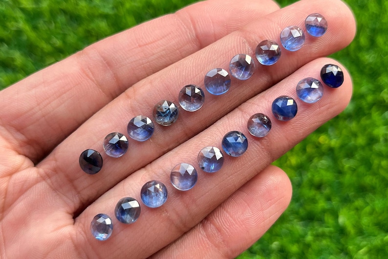 May include: A collection of 17 faceted round blue sapphires of varying shades, arranged in a gradient from light to dark blue.