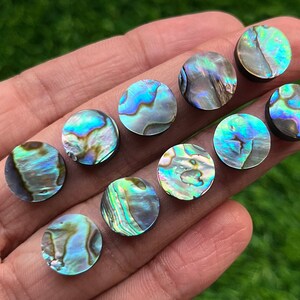 May include: Ten round iridescent abalone shell inlay pieces. The pieces are a variety of blues, greens, and purples with a black backing.