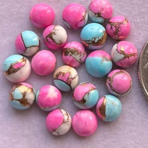 May include: A collection of round beads in shades of pink, blue, and white. Some beads have a marbled appearance with gold-colored veining. The beads are arranged closely together, creating a visually appealing display.
