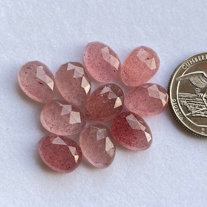May include: Ten faceted, pink quartz stones, each with a slightly different shade of pink, are arranged in a cluster on a white surface. A US quarter is included for size reference.