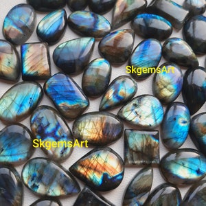 Könnte beinhalten: Eine Sammlung von irisierenden Labradorit-Cabochons in verschiedenen Formen und Größen. Die Steine haben eine blaue, grüne und goldene Farbe mit einem schimmernden Effekt. SkgemsArt ist auf dem Bild geschrieben.
