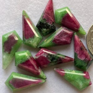 May include: A collection of faceted gemstones with a striking color contrast. The gems feature a vibrant combination of deep red and lush green hues. The shapes vary, with some having pointed tips and others with flat edges. The gemstones are arranged on a light-colored surface.