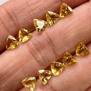 Könnte beinhalten: Eine Sammlung von 10 dreieckigen facettierten Edelsteinen in gelber Farbe. Die Edelsteine sind in einem Halbkreis auf einer Hand angeordnet.