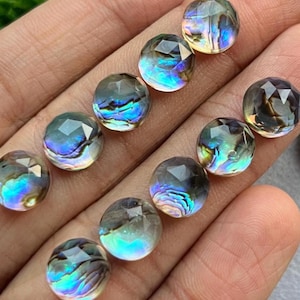 May include: A collection of iridescent, faceted gemstone beads. The beads are round with a clear, smoky color and display a range of colors including blue, green, and purple. The beads are held in a hand.