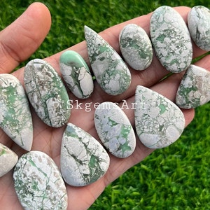 May include: A collection of 11 green and white cabochons, with a variety of shapes and sizes. The cabochons are smooth and polished, with a natural, organic look. SkgemsArt is printed on the image.