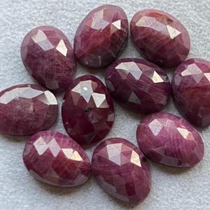 Puede incluir: Un conjunto de gemas facetadas de forma ovalada en varios tamaños. Las gemas muestran un tono rojo intenso y rico con patrones internos. Las superficies están talladas con múltiples facetas, creando un efecto brillante. Son gemas sueltas.