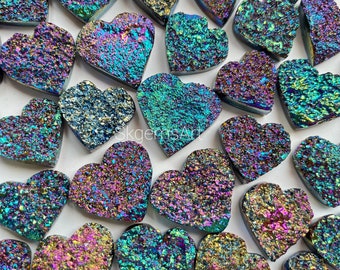 Op de afbeelding: Een verzameling van regenboogkleurige hartvormige stenen met een ruw, getextureerd oppervlak. De stenen zijn een mix van blauw, groen, paars en goud.