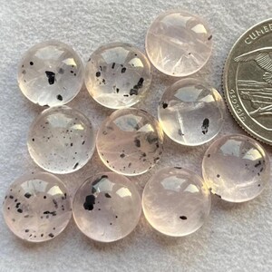 Könnte beinhalten: Zehn runde, durchscheinende, hellrosa Cabochons mit schwarzen Einschlüssen. Die Cabochons haben einen Durchmesser von etwa 2,5 cm.