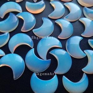 Peut inclure: Une collection de cabochons en opale irisée en forme de croissant de lune. Les cabochons sont de couleur bleu clair avec un reflet arc-en-ciel. Les cabochons sont dispersés sur une surface noire.
