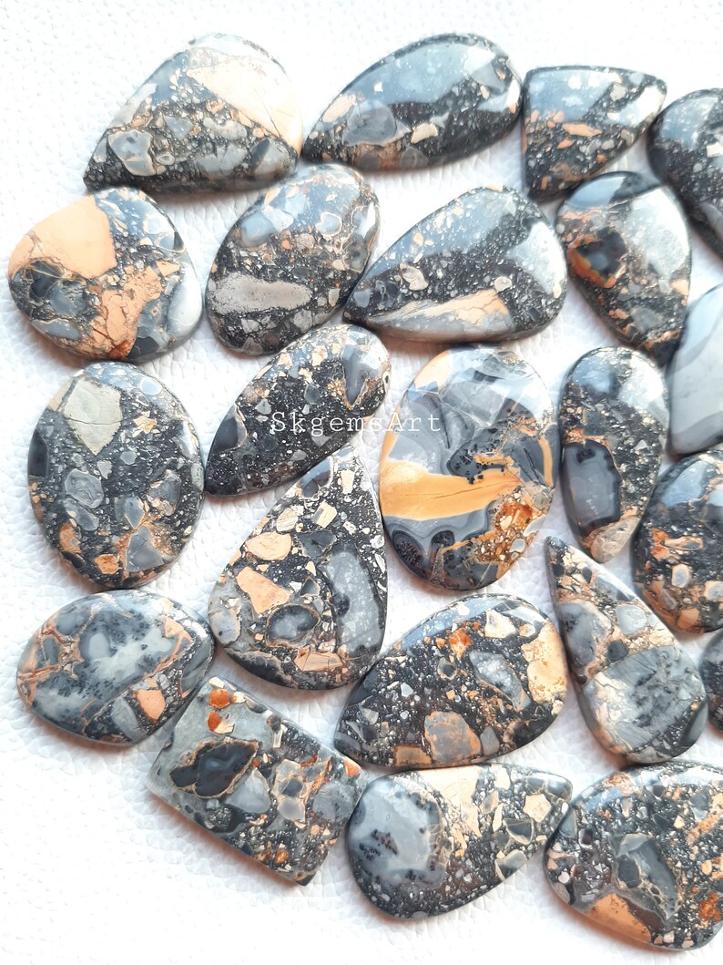 May include: A collection of 20+ natural stone cabochons in a variety of shapes and sizes. The stones are a mix of black, gray, and brown with a speckled pattern. The cabochons are perfect for jewelry making, crafting, and other creative projects.