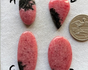 May include: Four cabochon cut pink and black rhodochrosite gemstones. The stones are labeled A, B, C, and D.