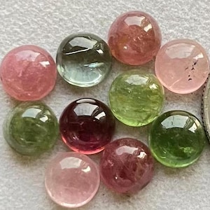 Könnte beinhalten: Sortiment aus zehn runden, cabochon geschliffenen Edelsteinen in verschiedenen Schattierungen von Rosa, Grün und Rot. Die Edelsteine haben einen Durchmesser von etwa 10 mm.
