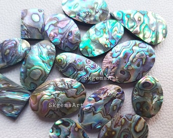Könnte beinhalten: Eine Sammlung von irisierenden Abalone-Muschel-Cabochons in verschiedenen Formen und Größen. Die Cabochons haben ein natürliches, organisches Muster in Blautönen, Grüntönen und Violett.
