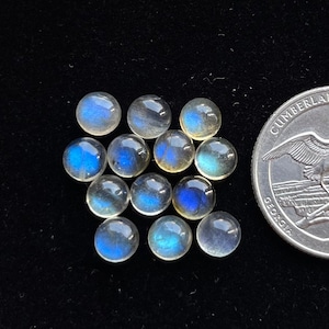 Può includere: Una collezione di 13 pietre preziose rotonde di labradorite iridescente, ciascuna con un diametro di circa 1,25 cm. Le pietre sono di colore blu chiaro con un bagliore iridescente brillante.