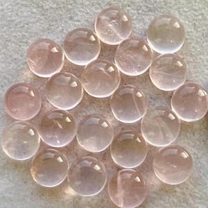 Könnte beinhalten: Eine Sammlung von 18 runden, durchscheinenden rosa Rosenquarz-Cabochons. Die Cabochons sind glatt und poliert, mit einem leichten Schimmer.