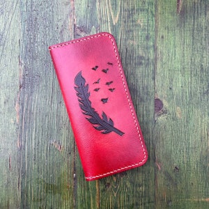 May include: A red leather wallet with a black feather and flock of birds design.