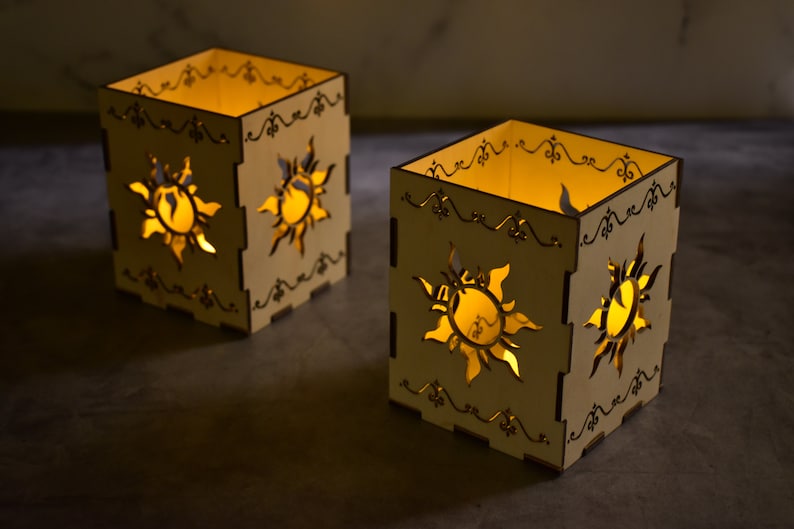May include: Two wooden candle holders with a sun design cut out. The candle holders are lit with a warm yellow glow.