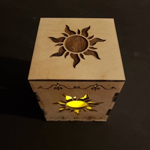 May include: A wooden box with a cutout design of a sun on the top and sides. The box is lit from inside, creating a warm glow.