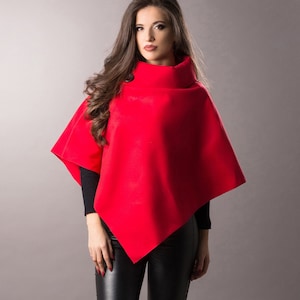 May include: A red poncho with a high neck and a long sleeve. The poncho is worn over black leggings and black heels.