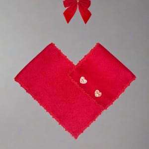 May include: A red velvet shawl with a lace trim and two heart-shaped buttons. A red velvet bow is on top of the shawl.