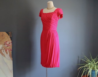 May include: A pink sleeveless dress with a square neckline and a gathered skirt. The dress is on a mannequin and has a gold necklace.