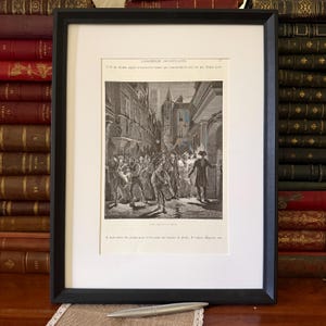 May include: A black framed print featuring a historical black and white engraving of a crowd in a narrow street. The text at the top reads L'ASSEMBLEE CONSTITUANTE and 77. The text at the bottom reads PARIS DANS LES RUES. The print is matted in white.