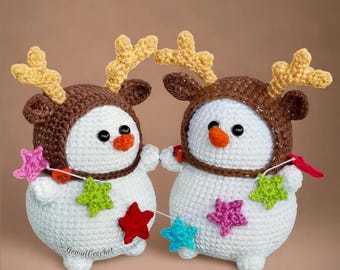 May include: Two crocheted snowman ornaments wearing brown reindeer hats with antlers. The snowmen are holding a string of colorful star-shaped ornaments.