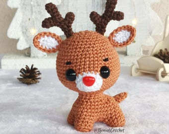 May include: A crocheted reindeer toy with brown antlers, a red nose, and big black eyes. The reindeer is standing on a white surface.