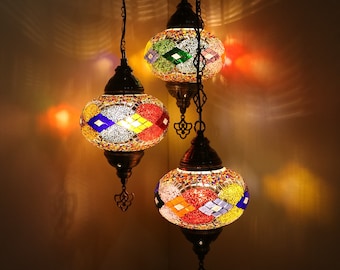 May include: A multi-tiered chandelier with three round, colorful mosaic glass globes. The globes are lit and cast a warm glow. The chandelier is made of metal and has a traditional design.